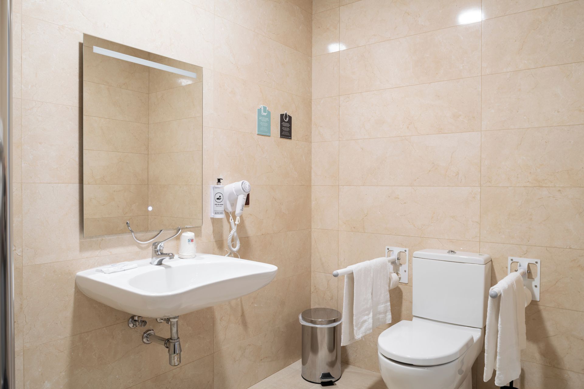 Un baño moderno con lavamanos, espejo, inodoro y toallero.