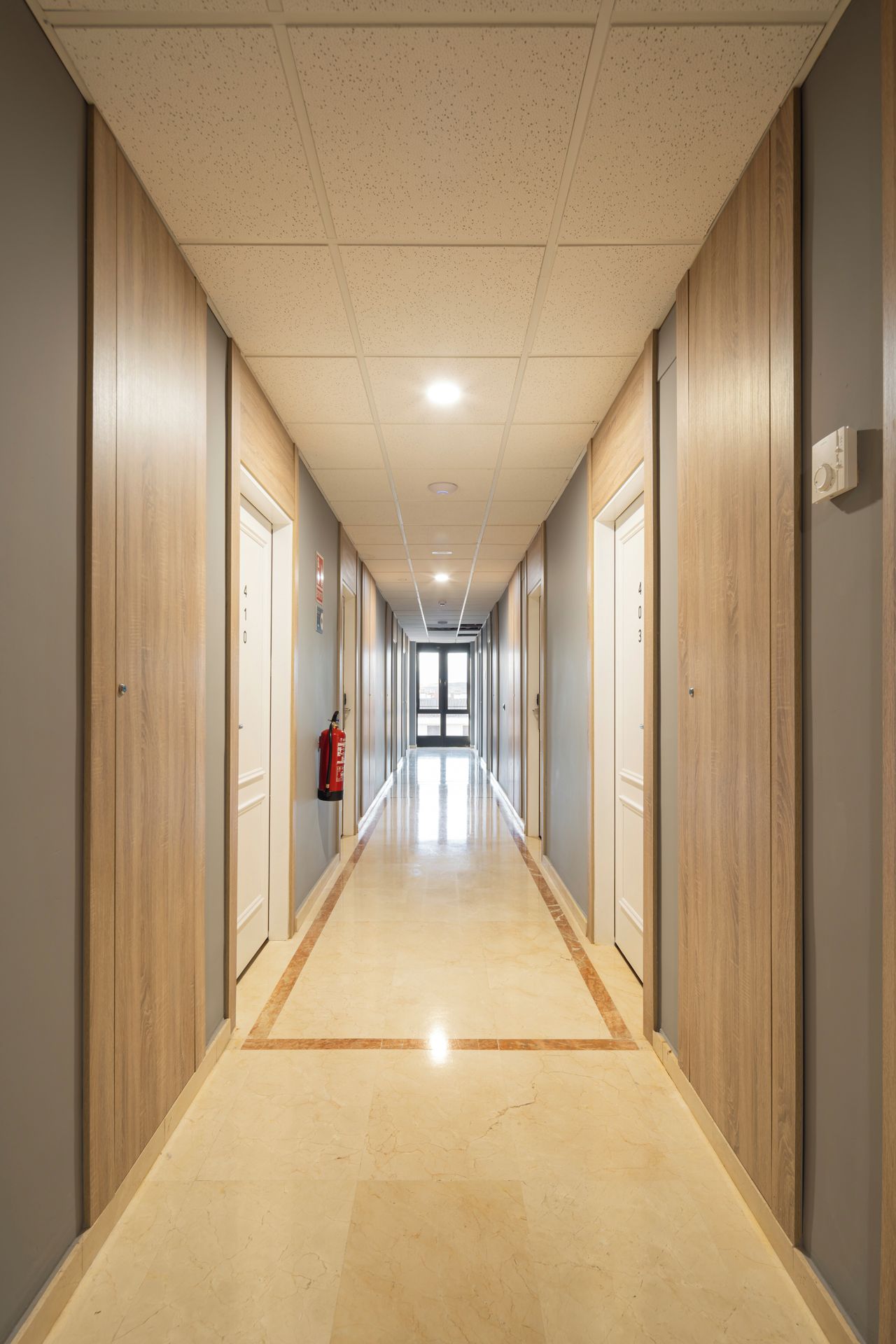 A long, narrow hallway with wooden paneling on the walls and a tiled floor.