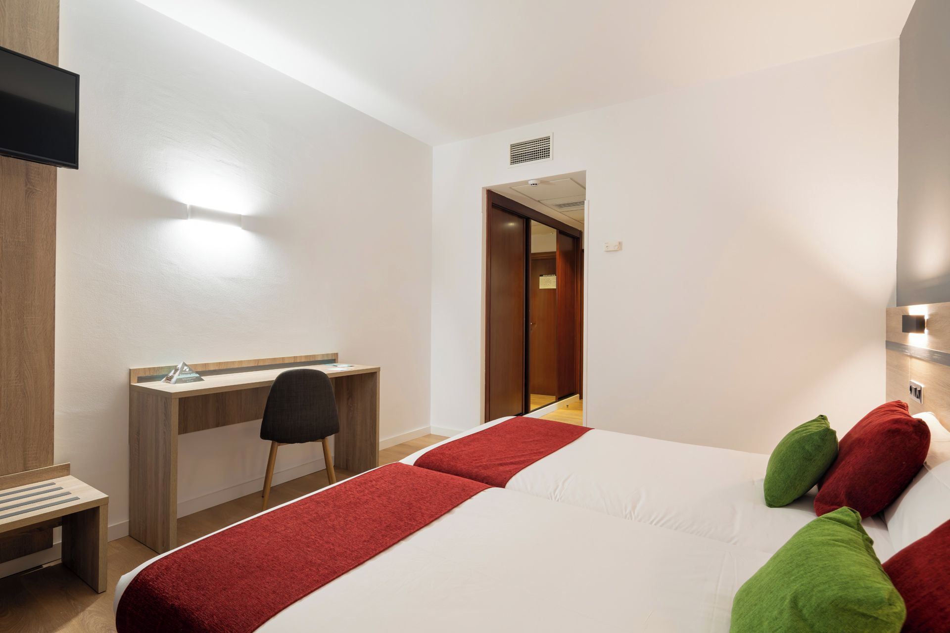 A hotel room with a bed, a desk, a chair, and a television.