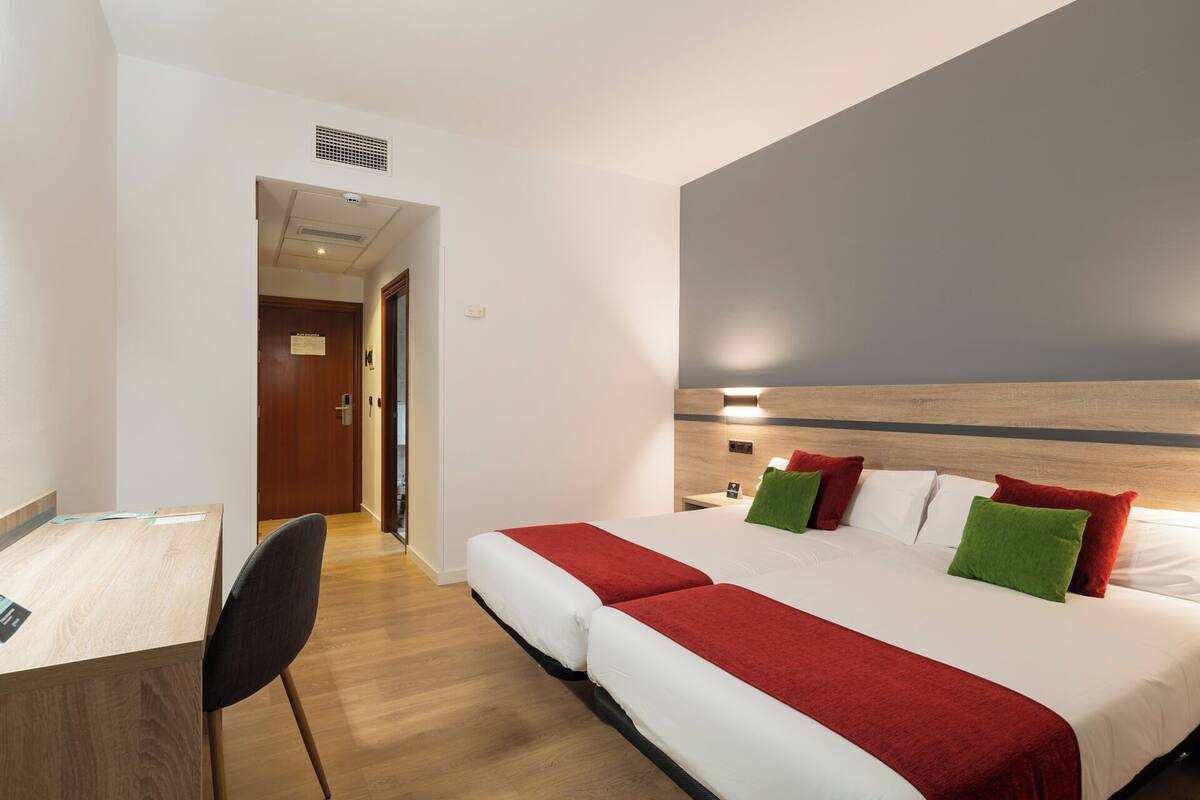 A hotel room with a bed, bedside table, chair, and a desk.