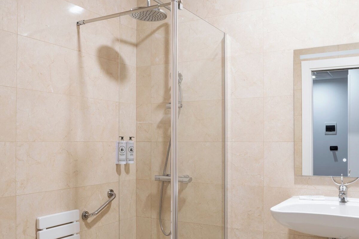 A modern bathroom with a glass-enclosed shower, a white sink, and a towel rack.