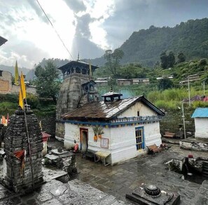 A traditional building with a tiled roof, a small porch, and a stone structure nearby. - Triyuginarayan Maangal Resort  (Ukhimath)