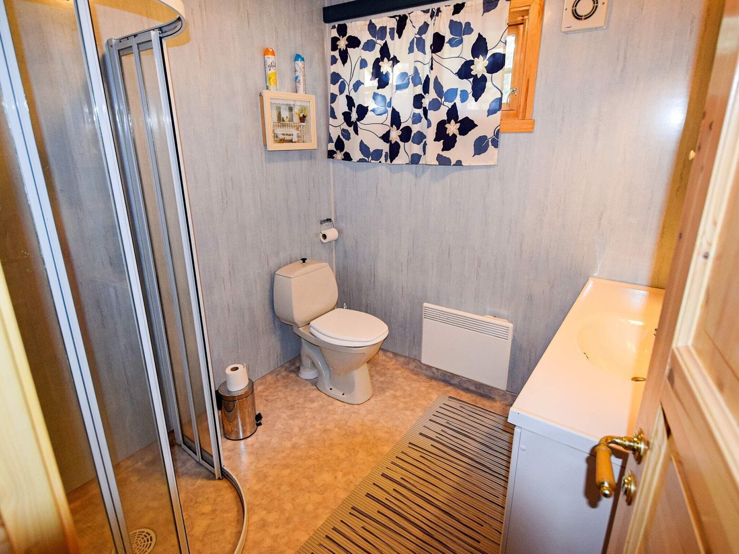 A bathroom with a toilet, a shower, a radiator, and a small shelf with toiletries.