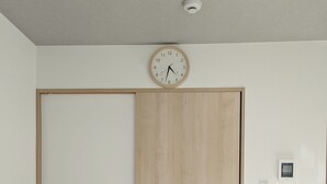A bedroom with a bed, a wooden wardrobe, a wall clock, a Wi-Fi sign, and a thermostat. - sun seinibannkan 101 (Osaka)