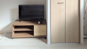 A room with a flat-screen TV on a wooden stand, a wardrobe with a sliding door, and an air conditioning unit mounted on the wall. - sun seinibannkan 101 (Osaka)