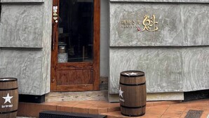 A building with a black and grey facade, a wooden door, and two barrels in front. - sun seinibannkan 101 (Osaka)