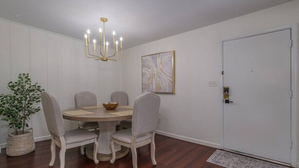 Un coin repas comprenant une table ronde, six chaises, un lustre, une plante en pot et une porte.