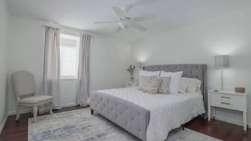 Une chambre à coucher comprenant un lit, une chaise, une table de chevet, une lampe et un ventilateur de plafond.