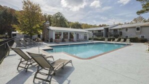 Une piscine avec des chaises longues, un espace de détente couvert et un bâtiment doté de balcons.