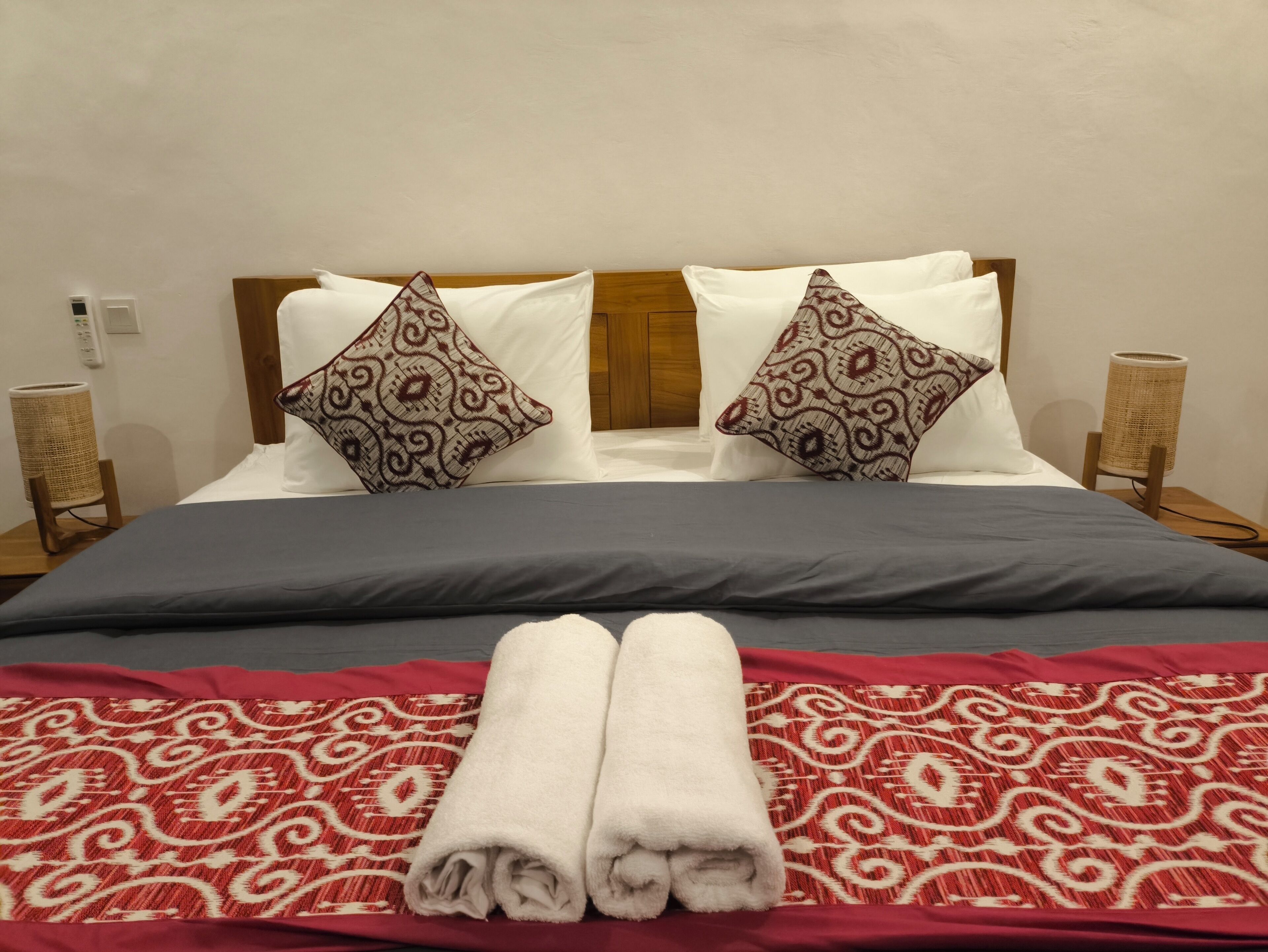 Een net opgemaakt bed met een rood-wit gebed eiland, twee decoratieve kussens en een paar opgevouwen witte handdoeken.