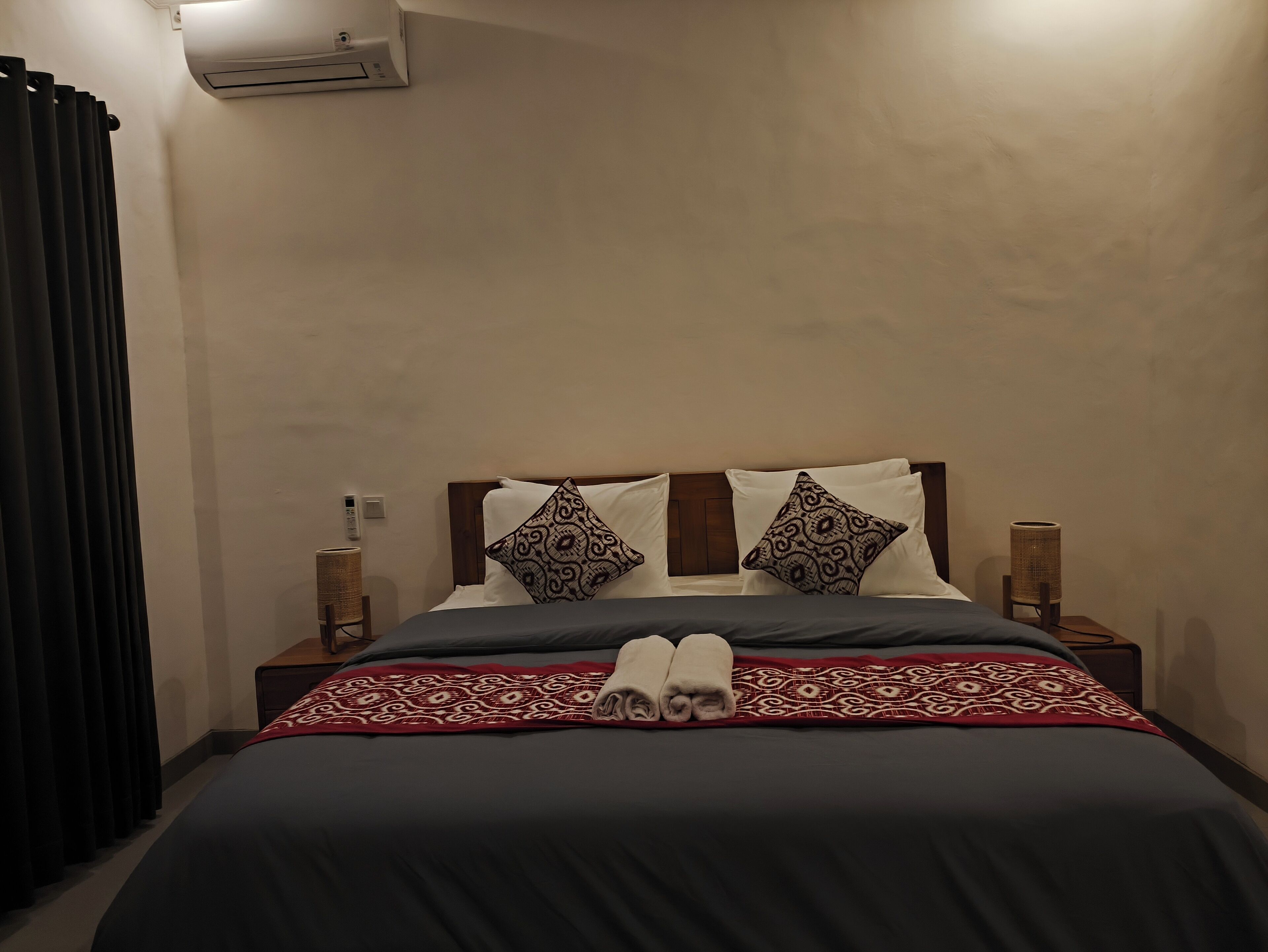 A neatly made bed with patterned pillows, a red and white throw blanket, and two bedside lamps.
