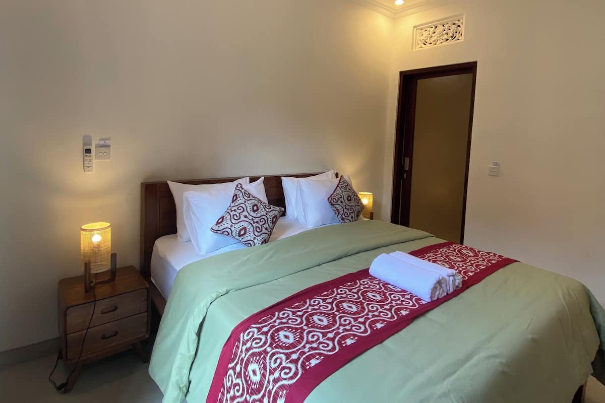 A neatly made bed with a patterned bedspread, a bedside lamp, and a nightstand with a drawer.