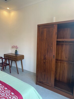 A bedroom with a bed, a wooden wardrobe, a desk with a chair, and a small table with a potted plant.