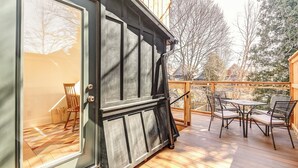 Une terrasse en bois avec des meubles d’extérieur, une porte-fenêtre coulissante et une vue sur les arbres et les maisons.
