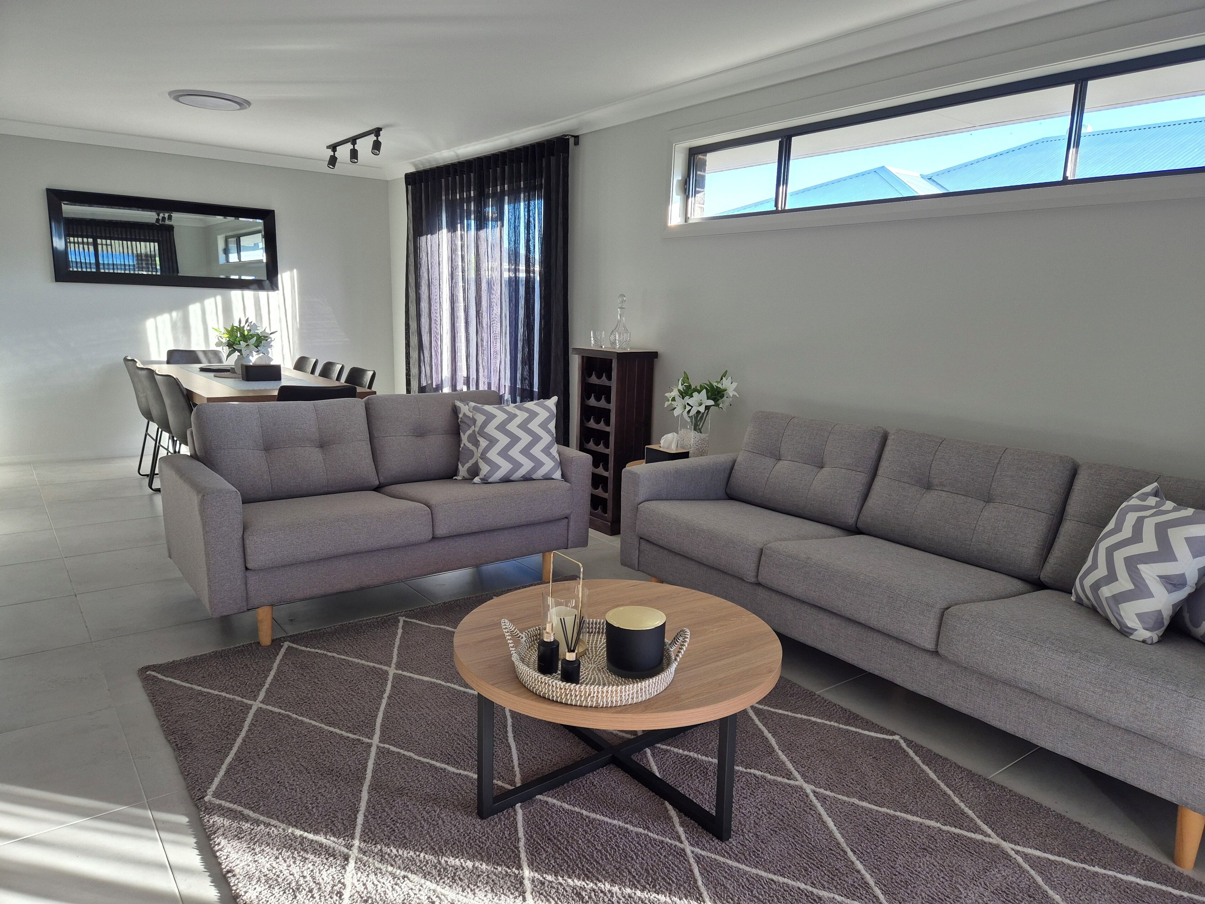 A modern living room with two grey sofas, a coffee table, and a dining area with chairs and a table.