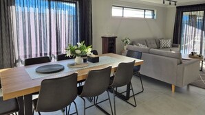 Una sala de estar moderna con comedor, que incluye un sofá, una mesa de comedor con sillas y ventanas grandes con cortinas.