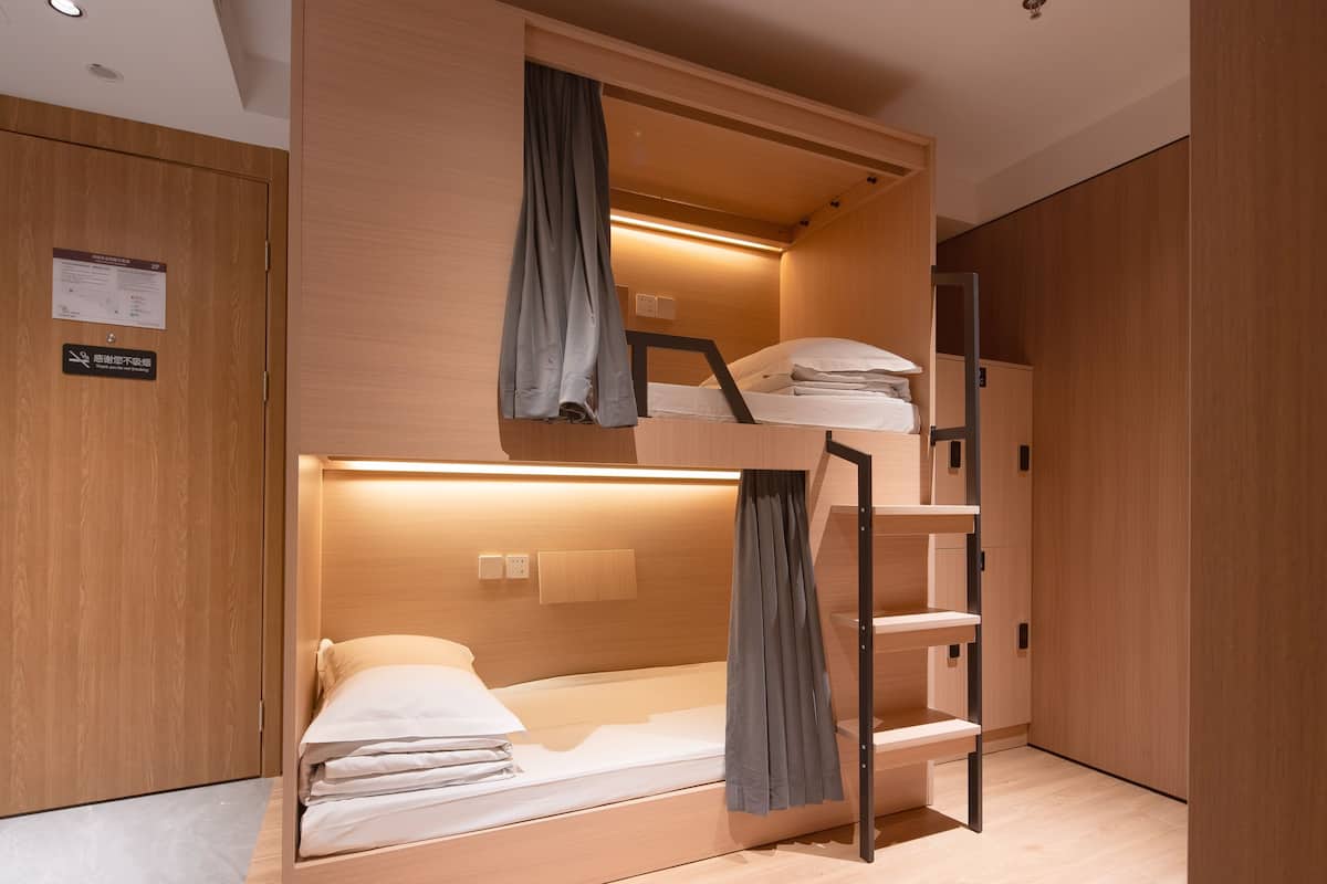A bunk bed room with a wooden finish, a small desk, and a wardrobe.