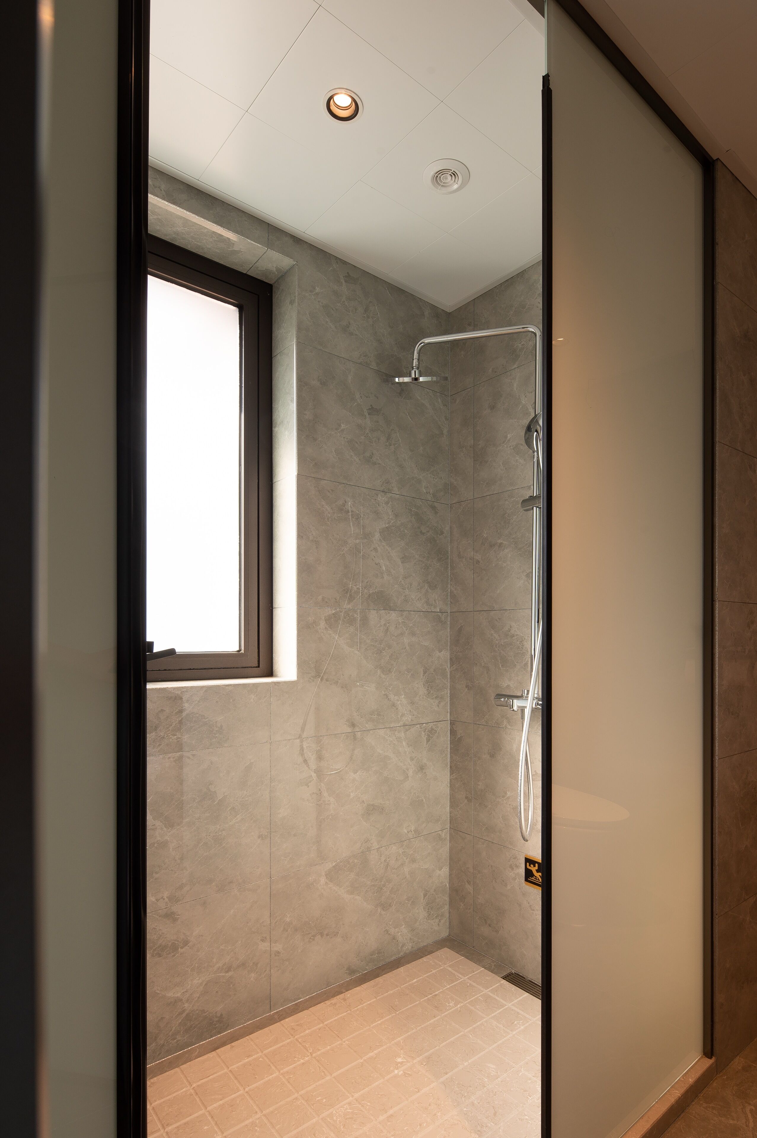 A modern shower area with a glass door, a window, and a ceiling light.
