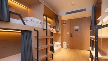 Habitación de hotel pequeña con literas, suelo de madera y estanterías empotradas.