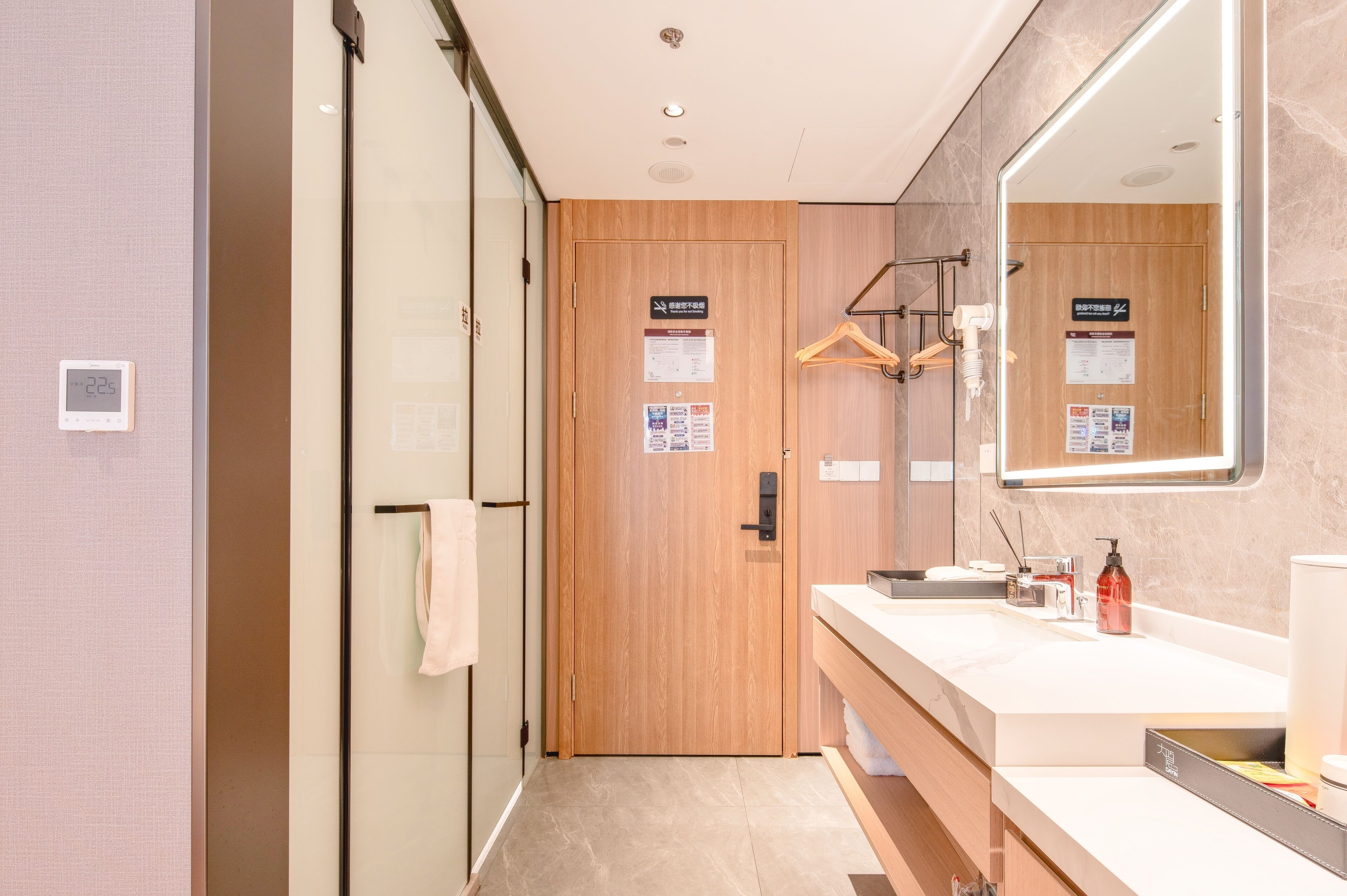 A modern bathroom with a wooden door, a large mirror, and a white sink with toiletries.