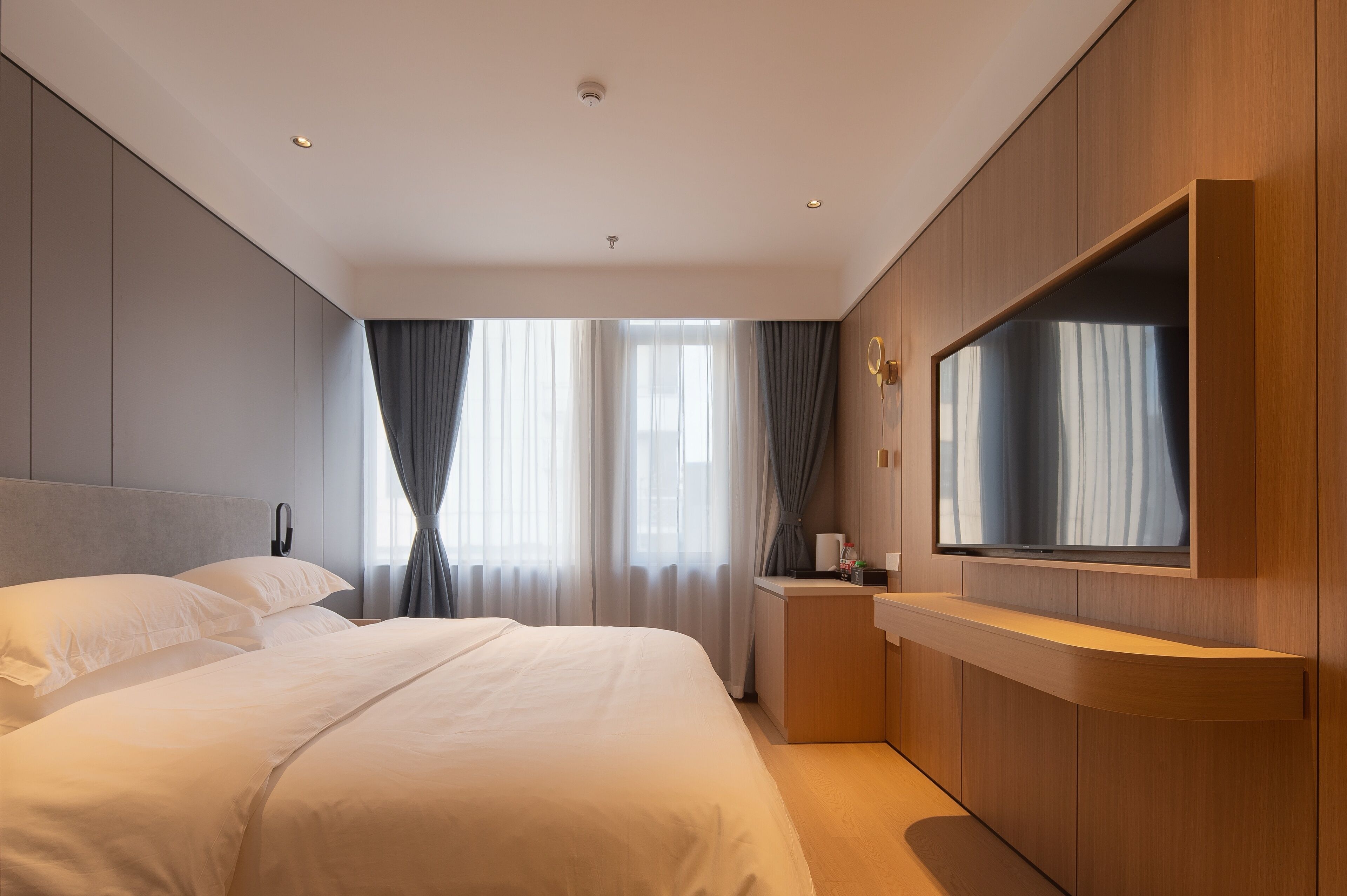 A modern hotel room with a large bed, a flat-screen TV mounted on the wall, and a small bedside table.
