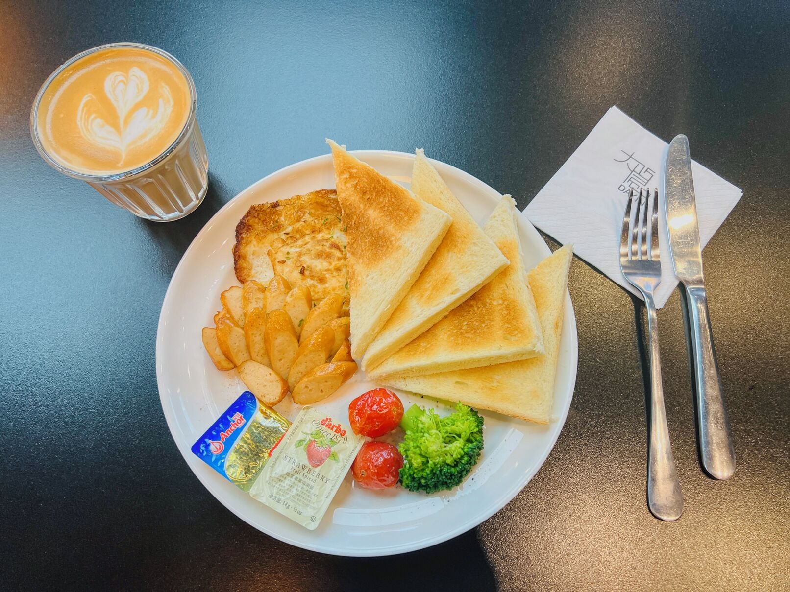 Un plato con tostadas, papas, fresas, brócoli y un vaso de café sobre una mesa.