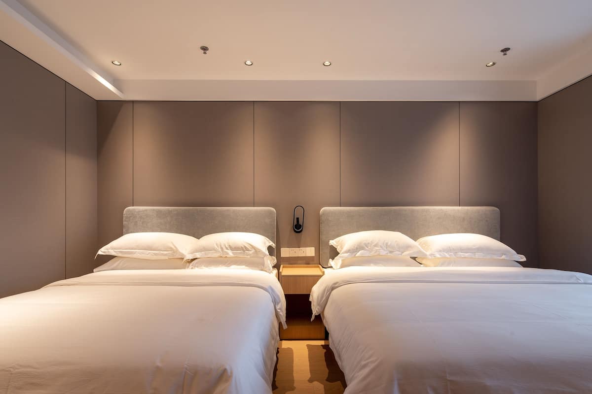 A modern hotel room with two beds, a neutral color scheme, and recessed ceiling lighting.