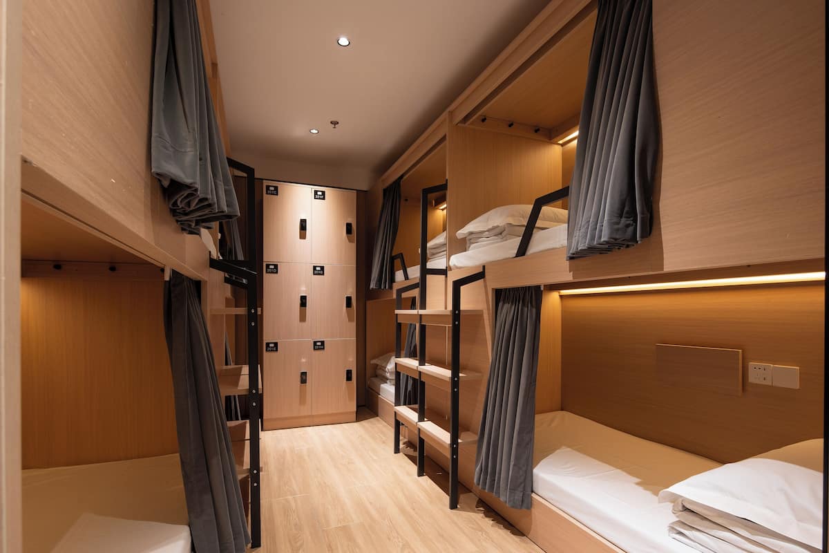 A compact, modern hotel room with bunk beds, a wooden wardrobe, and a small seating area.