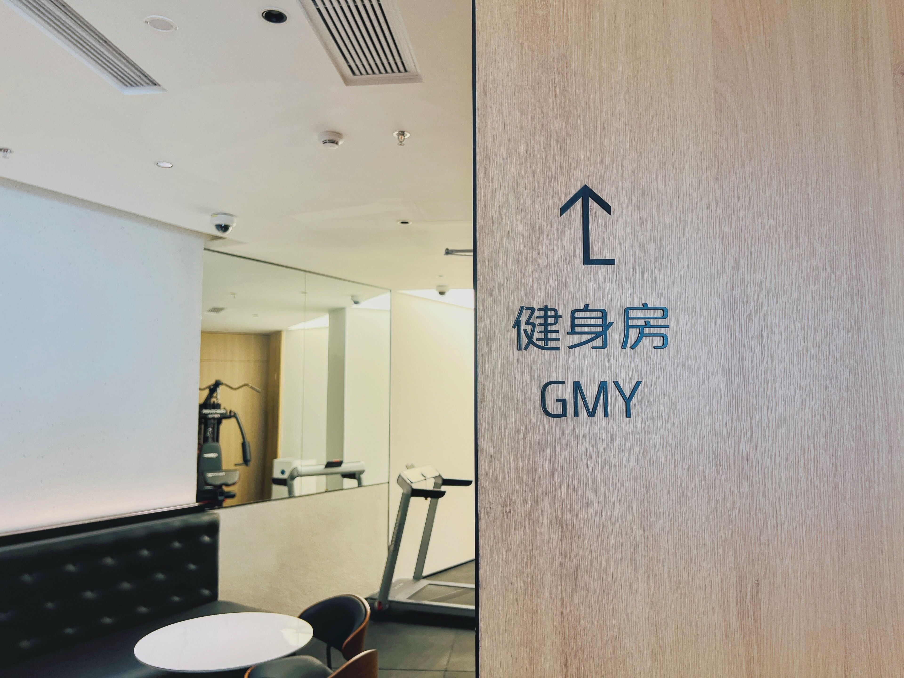 A modern fitness center with a treadmill, a mirrored wall, and a sign indicating the direction to the gym.