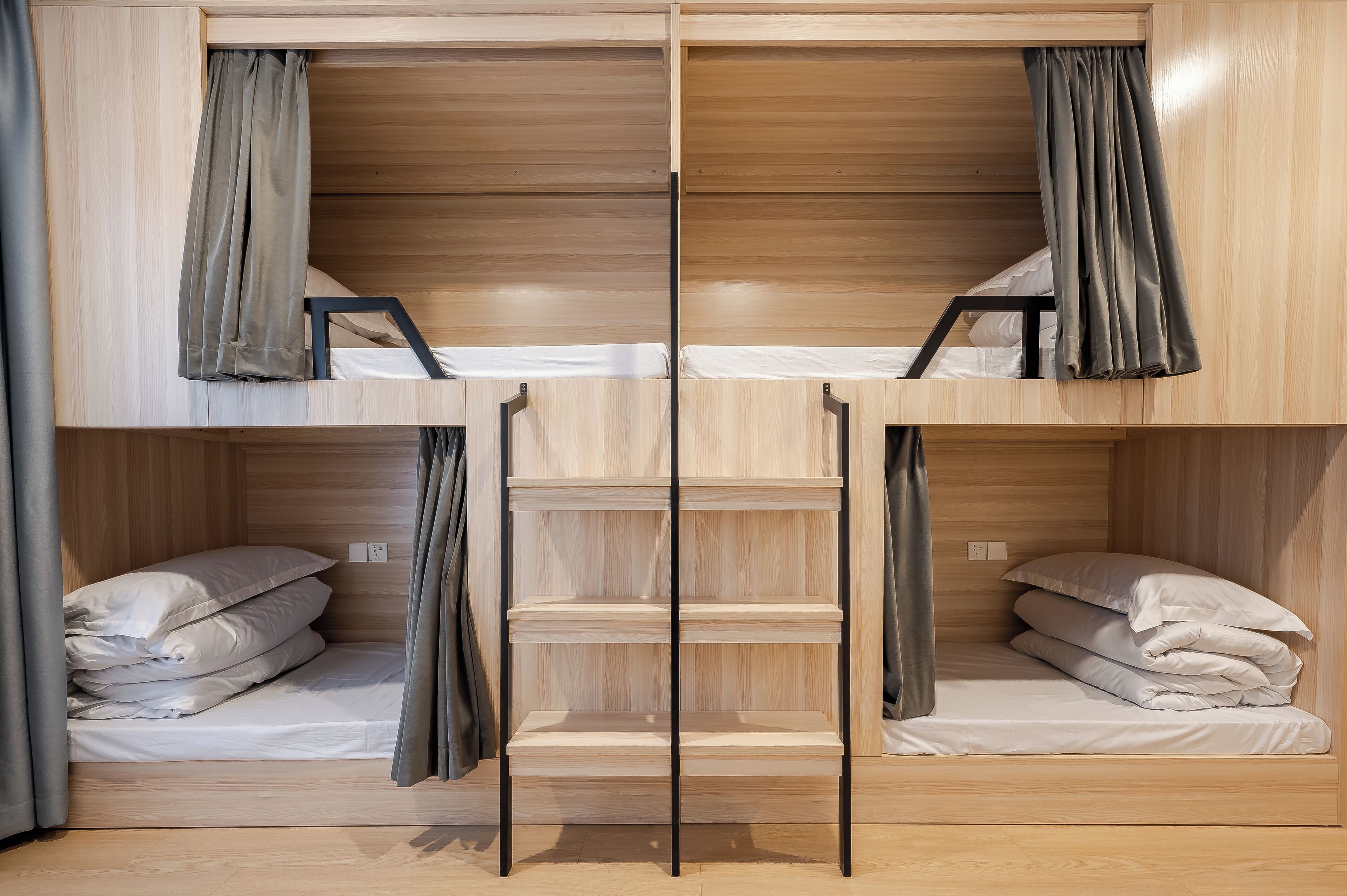 A bunk bed room with wooden walls and curtains. There are two beds, each with a pillow and a blanket.