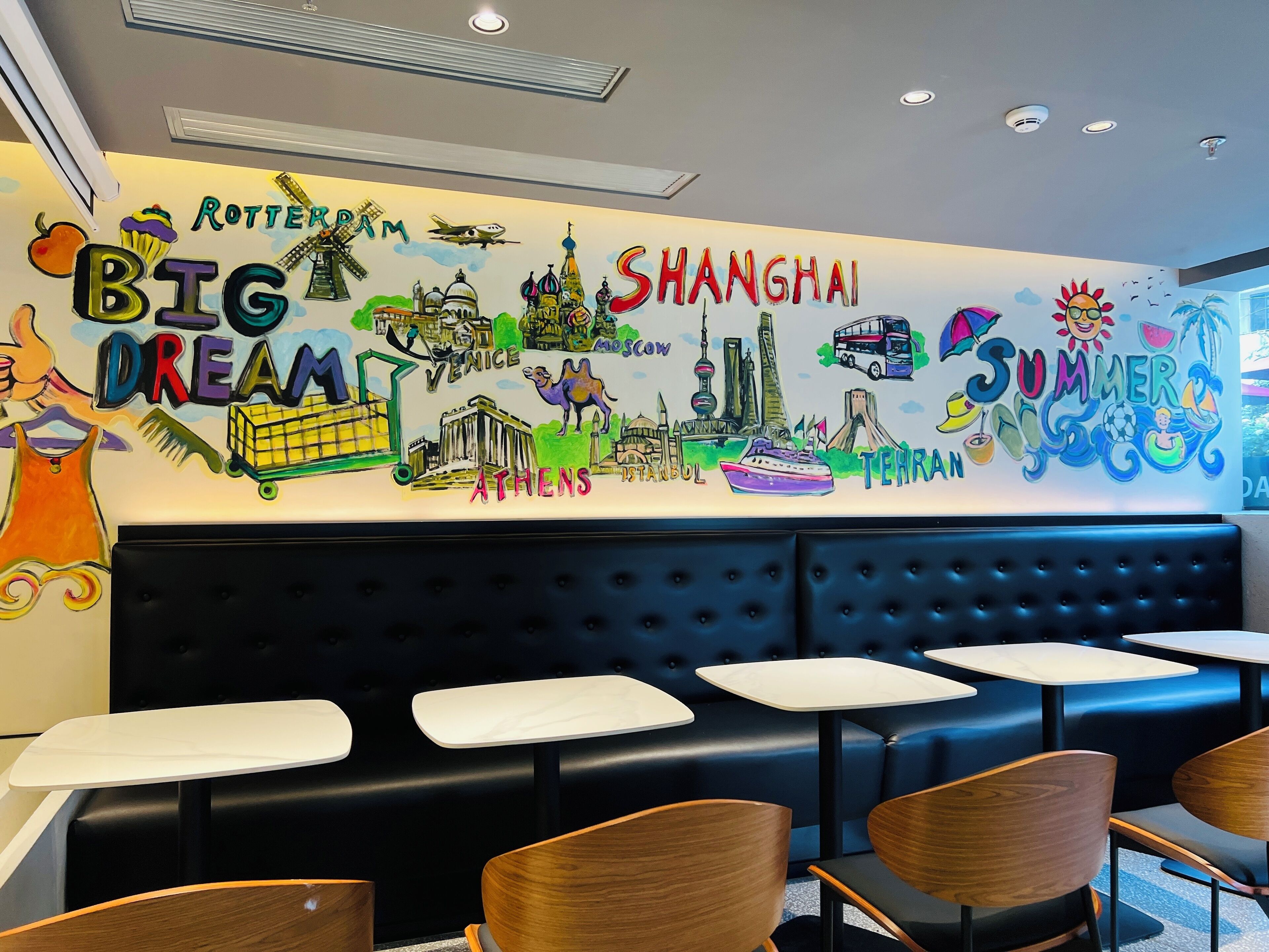 Een restaurantinterieur met een muurschildering van stadslandmarken en de tekst 'BIG DREAM' en 'SUMMER'.