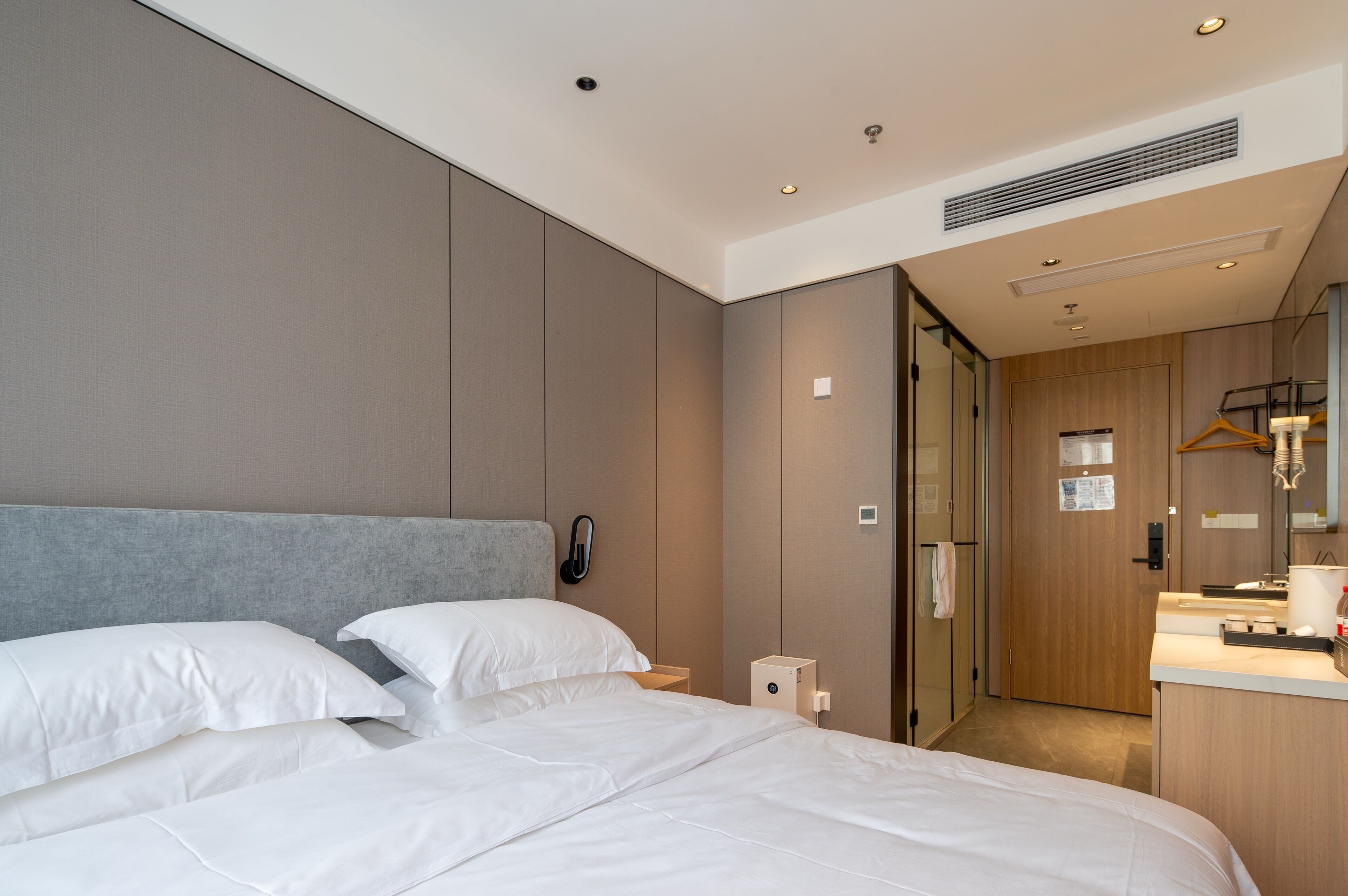 A hotel room with a large bed, a bedside table, a mirror, and a door leading to a bathroom.