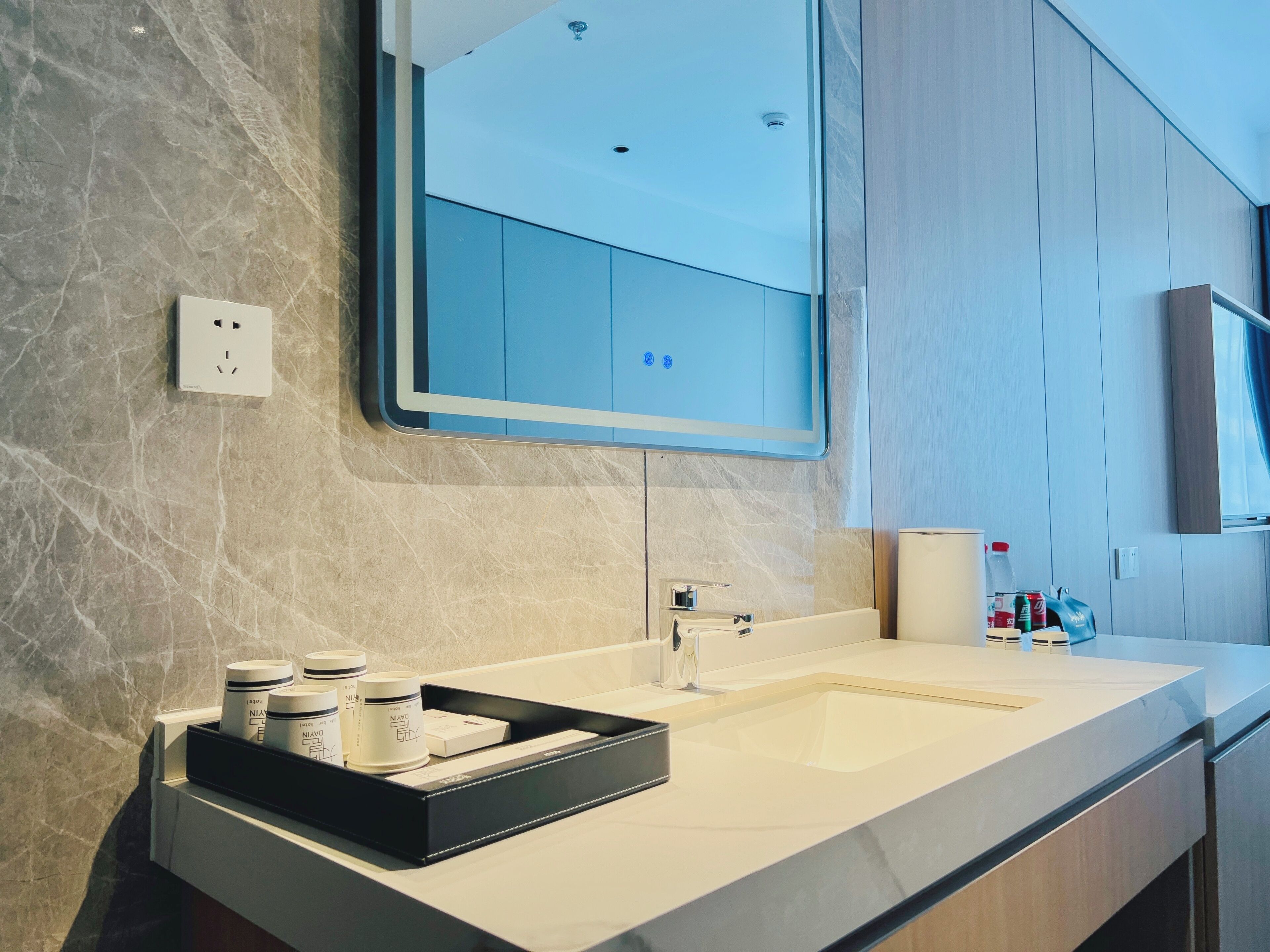 Un baño moderno con encimera de mármol, un espejo grande, un lavabo y una bandeja negra con artículos de aseo.
