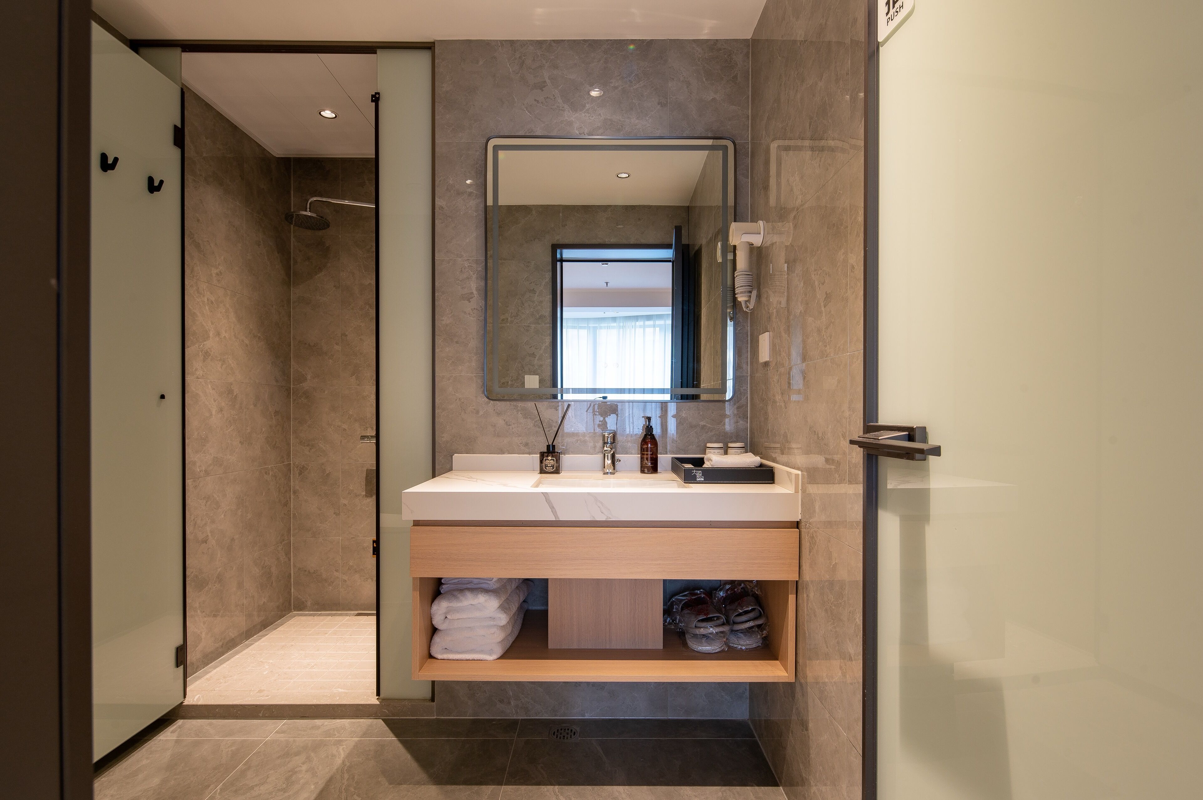 A modern bathroom with a glass shower enclosure, a large mirror, and a vanity with a sink and storage.