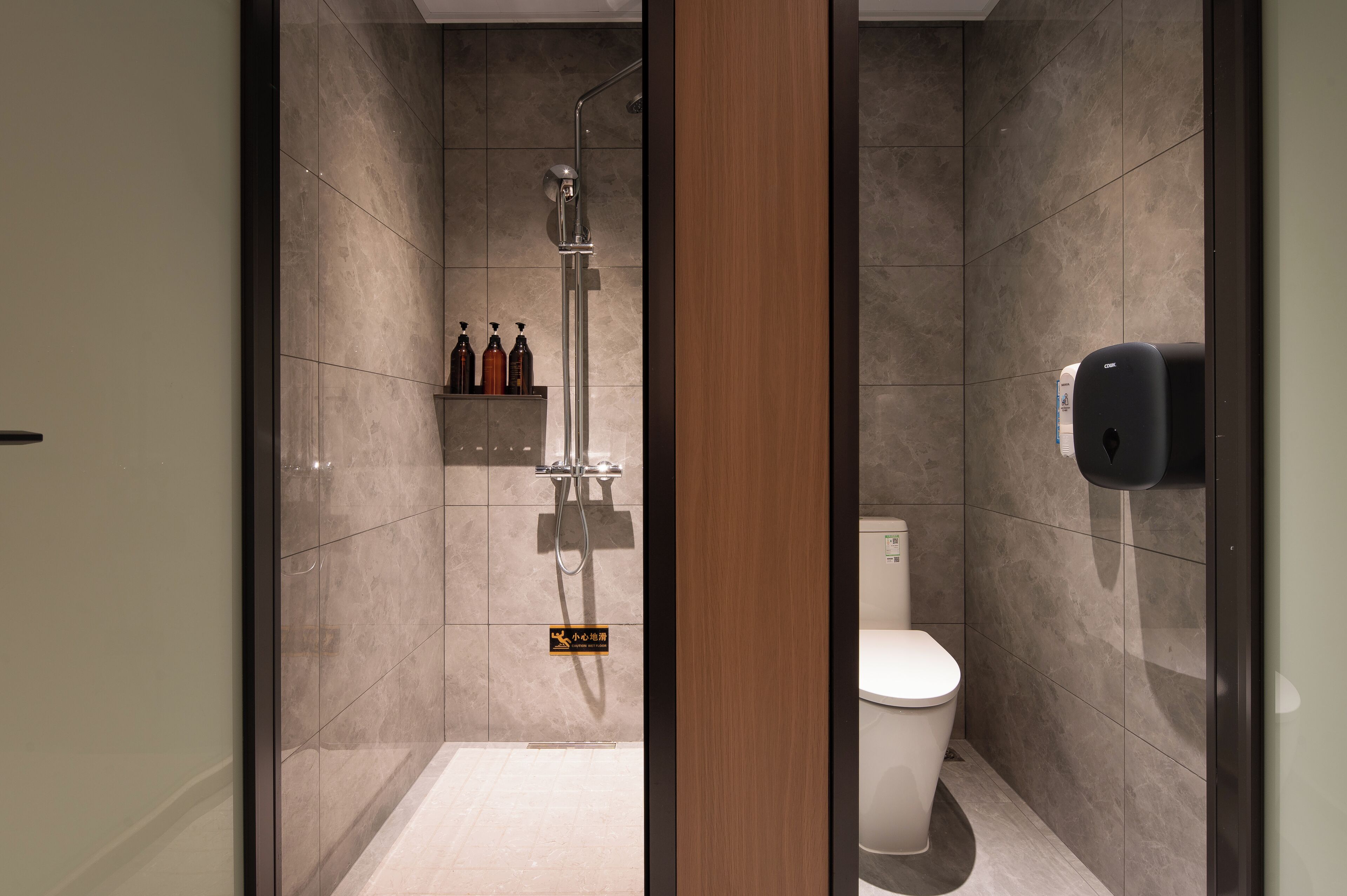 A modern bathroom with a shower, toilet, and hand sanitizer dispenser.