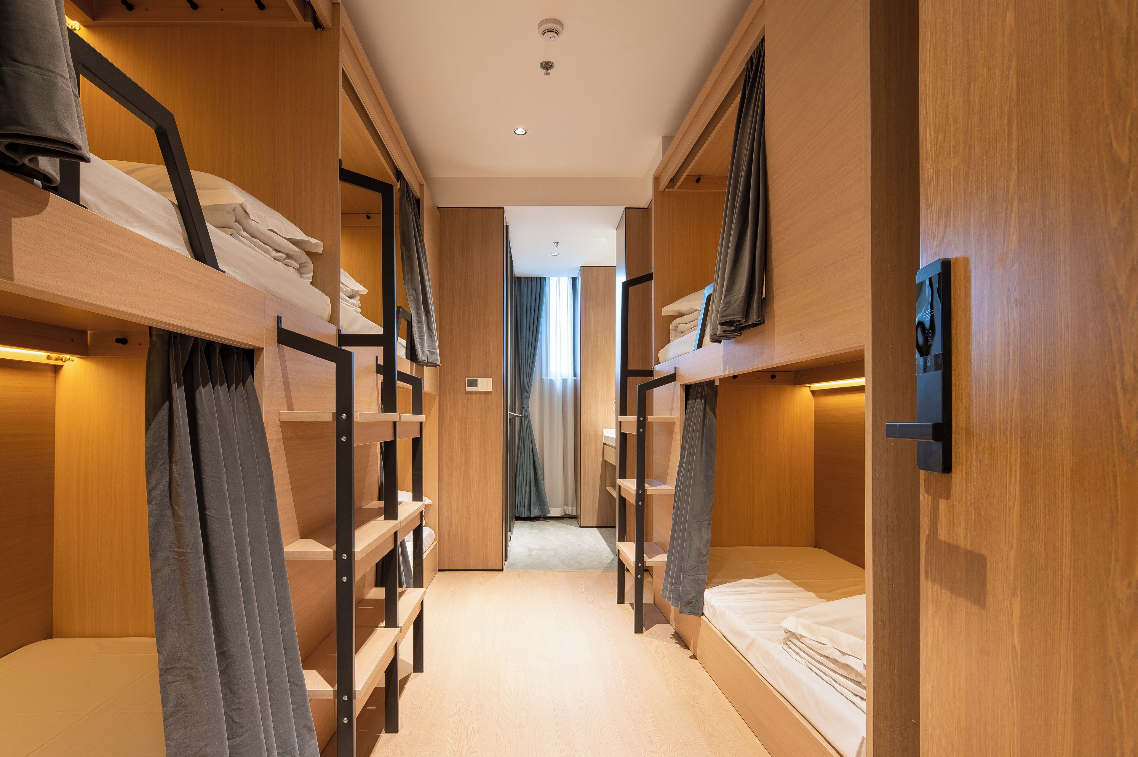 A hotel room with bunk beds, wooden walls, and a corridor leading to a bathroom.
