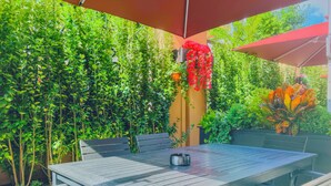 An outdoor patio with a wooden table and chairs, surrounded by lush greenery and red flowers. - Dayin Serene Garden Hotel - Shanghai Jing'an Joy City Suzhou Creek (Shanghai)