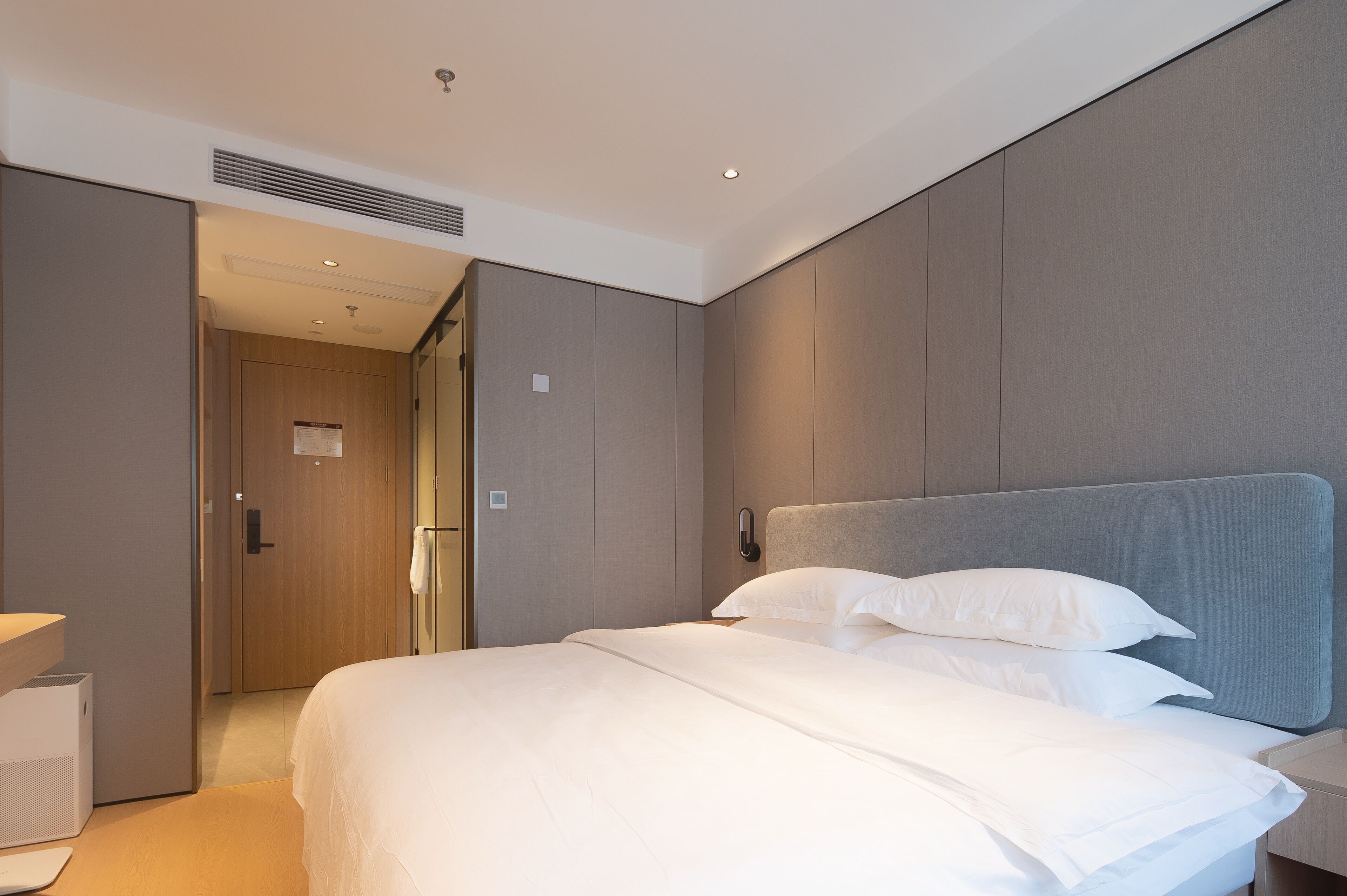 A modern hotel room with a large bed, a bedside table, and a wardrobe.