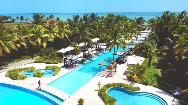 A resort with multiple swimming pools, palm trees, and a view of the ocean.