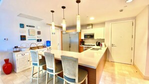 A modern kitchen with a central island, bar stools, a refrigerator, microwave, and a sink.
