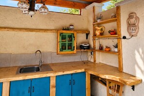 A kitchen with a wooden countertop, blue cabinets, a green-framed cabinet, and a wall-mounted shelf with decorative items.