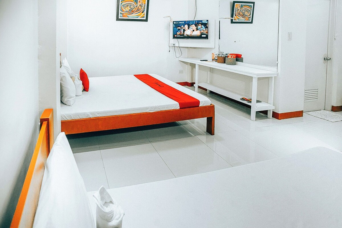 A hotel room with a bed, a white wall, a TV mounted above it, and a white door.