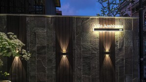 Een modern gevelontwerp met een stenen muur en houten panelen, met een bord waarop staat 'Villa Aashiyana'.