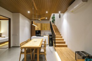 A modern kitchen with wooden cabinets, a dining area with a wooden table and chairs, and a staircase leading to an upper level. - Villa Aashiyana (Canggu)
