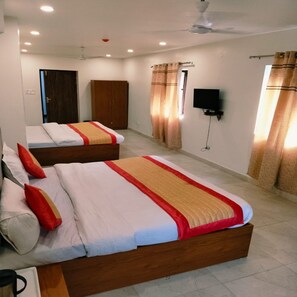 Une chambre d’hôtel avec deux lits, une armoire, une télévision et un ventilateur de plafond.