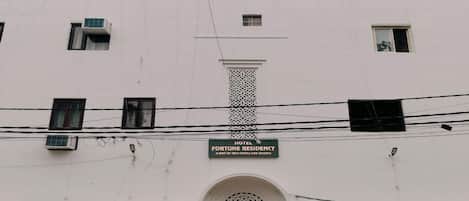 A building with a sign reading "FORTUNE RESIDENCY" and a "PARKING" sign. There are potted plants in front and a scooter parked outside.