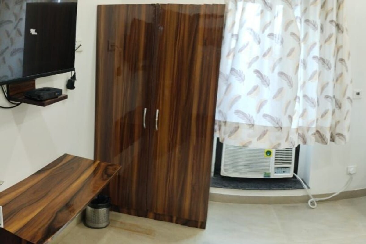 Une chambre d’hôtel avec une armoire en bois, un lit avec une literie blanche et des oreillers rouges, une table de chevet, un miroir et un téléviseur posé sur un meuble.