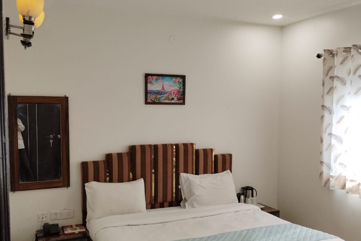 Une chambre avec un lit en bois, une table de chevet, une lampe fixée au mur, un ventilateur de plafond et un tableau encadré accroché au mur.