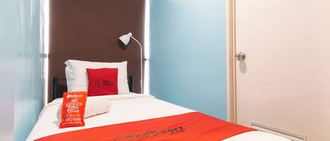 Una habitación de hotel con una cama, un almohadón rojo, una colcha roja y un almohadón blanco.
