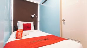 Een hotelkamer met een bed, een rood kussen, een rode deken en een wit kussen.